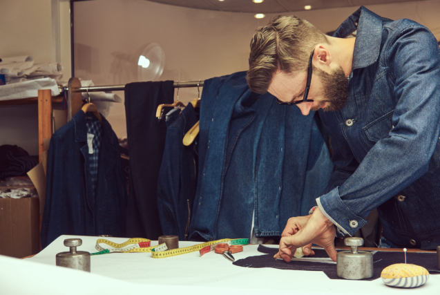 Handsome bearded tailor working with cloth samples at a sewing workshop.